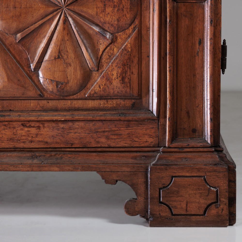 A large seventeenth-century Italian walnut cabinet featuring two tall panelled doors with carved geometric star relief motifs, framed by moulded side pilasters and resting on bracket feet. View VI