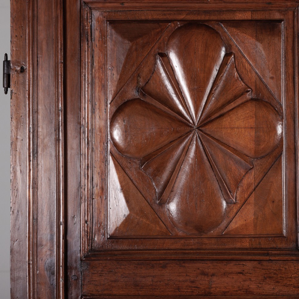 A large seventeenth-century Italian walnut cabinet featuring two tall panelled doors with carved geometric star relief motifs, framed by moulded side pilasters and resting on bracket feet. View VII