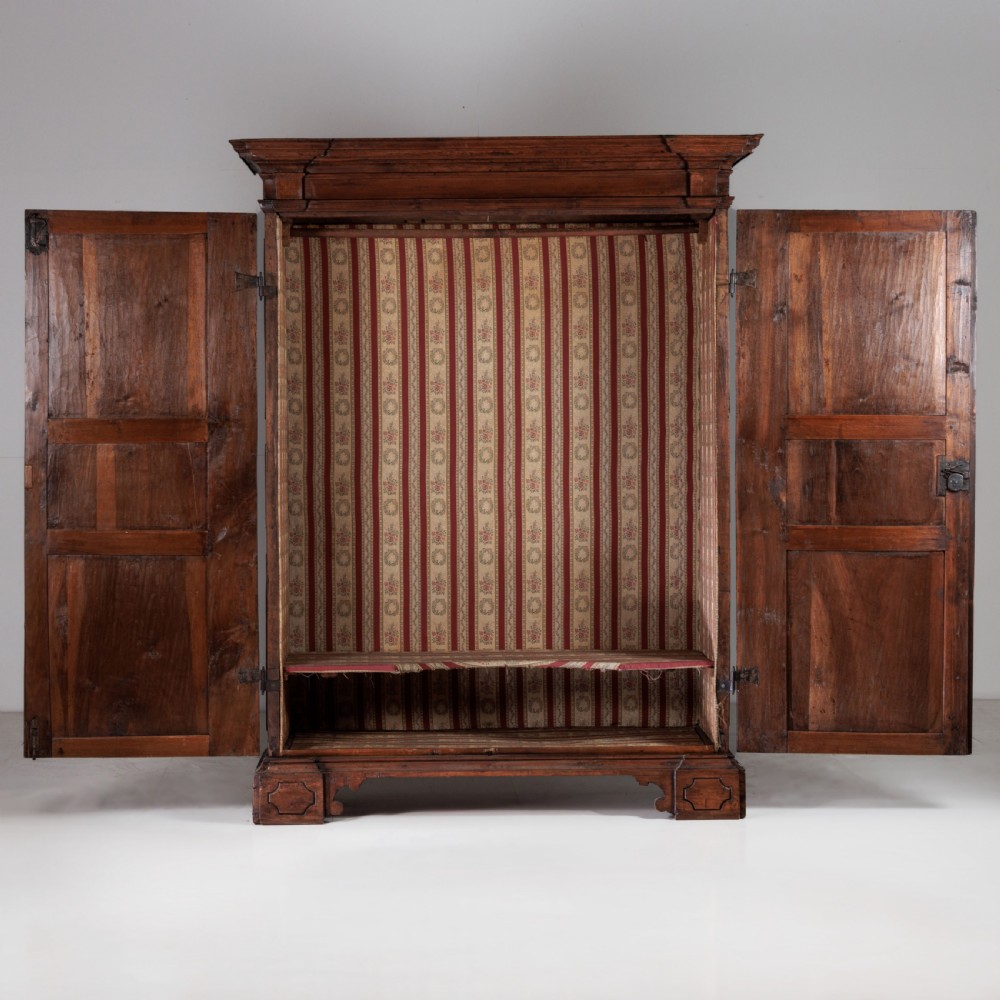 A large seventeenth-century Italian walnut cabinet featuring two tall panelled doors with carved geometric star relief motifs, framed by moulded side pilasters and resting on bracket feet. View X