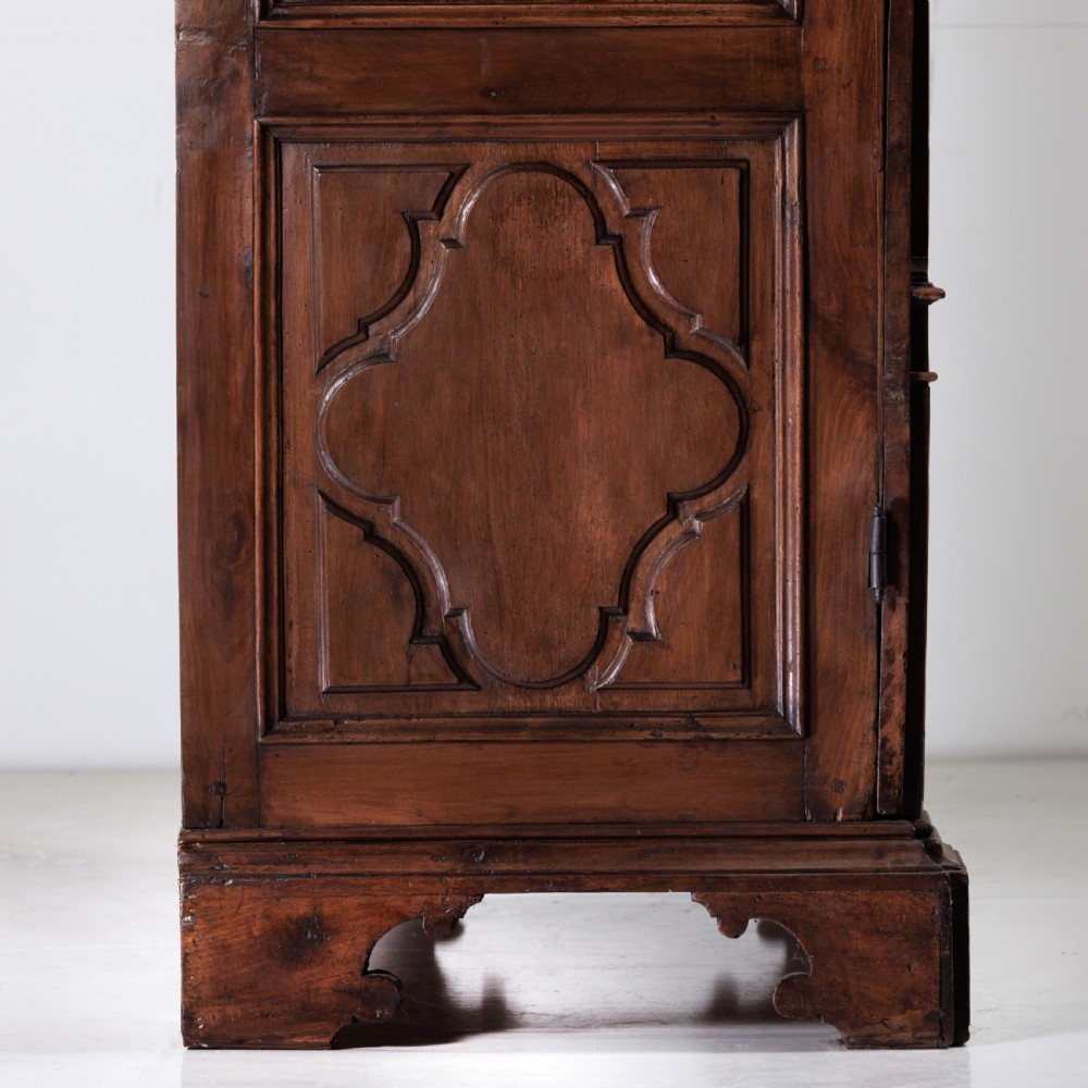 A large seventeenth-century Italian walnut cabinet featuring two tall panelled doors with carved geometric star relief motifs, framed by moulded side pilasters and resting on bracket feet. View XI