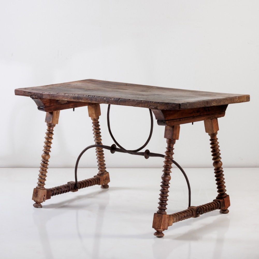 An 18th-century Spanish walnut trestle table featuring a solid timber top, spool-turned legs, and a curved wrought iron stretcher.