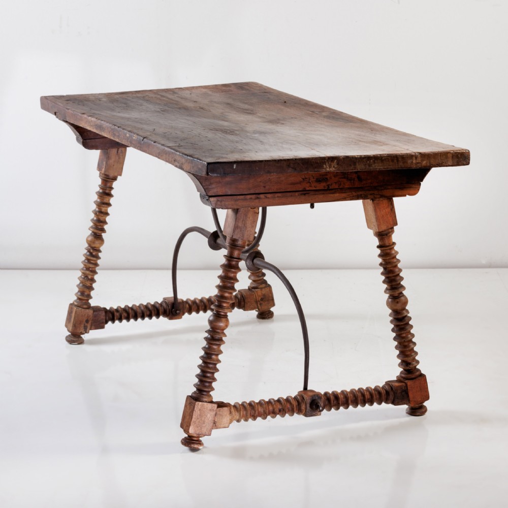 An 18th-century Spanish walnut trestle table featuring a solid timber top, spool-turned legs, and a curved wrought iron stretcher. View VI