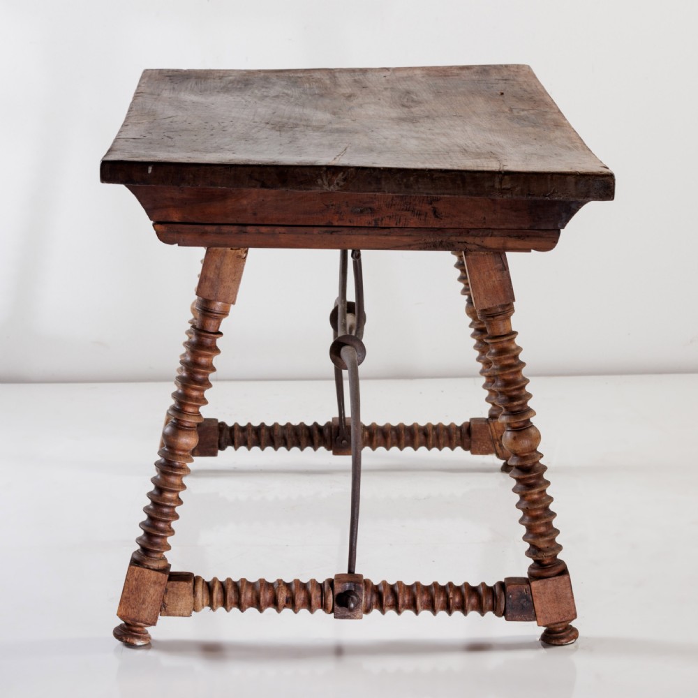An 18th-century Spanish walnut trestle table featuring a solid timber top, spool-turned legs, and a curved wrought iron stretcher. View X