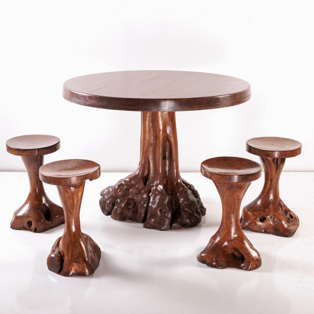 A round olive wood table with a natural tree root pedestal base surrounded by four matching root wood stools.