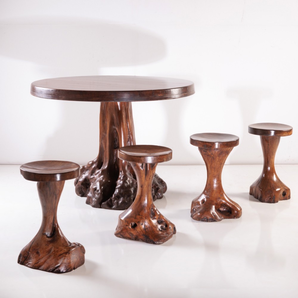 A round olive wood table with a natural tree root pedestal base surrounded by four matching root wood stools. View II