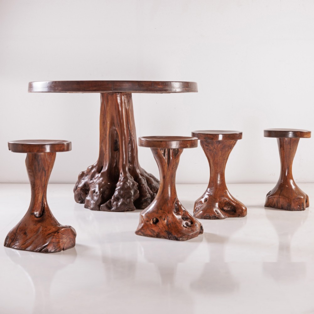 A round olive wood table with a natural tree root pedestal base surrounded by four matching root wood stools. View III