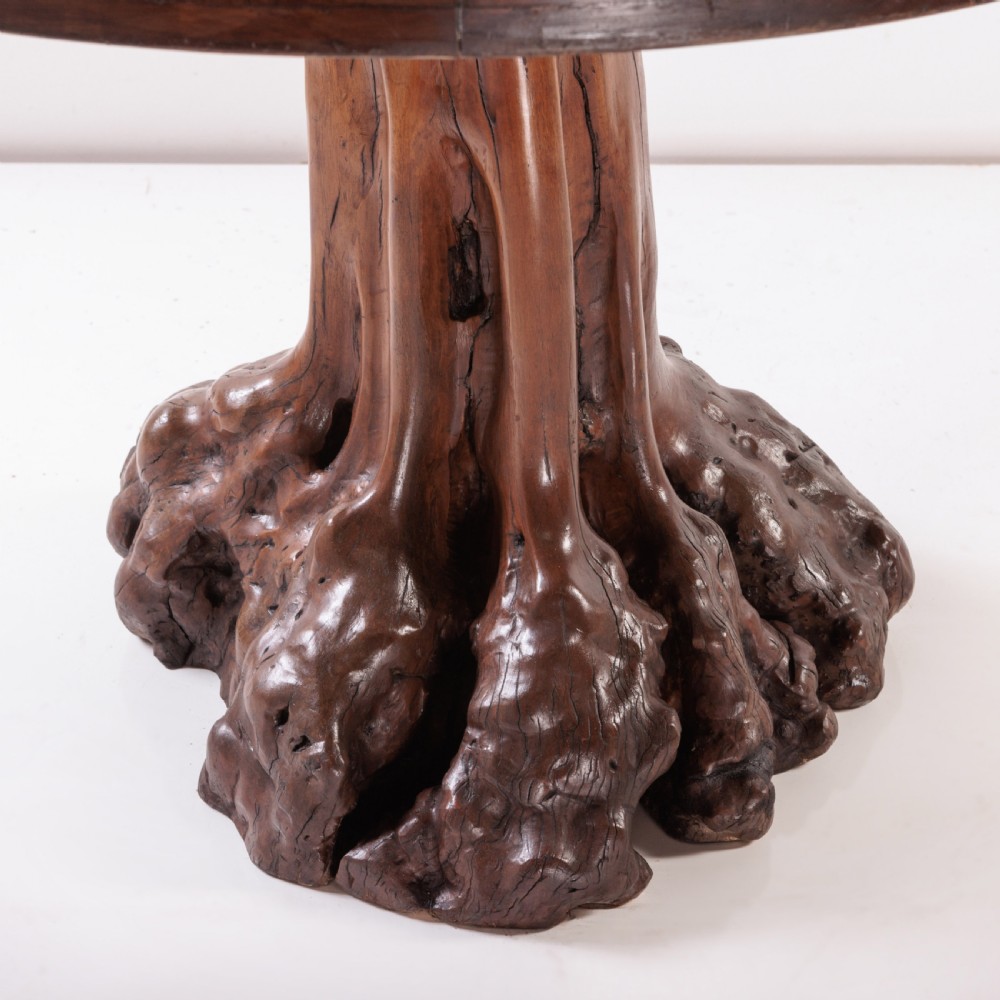 A round olive wood table with a natural tree root pedestal base surrounded by four matching root wood stools. View V
