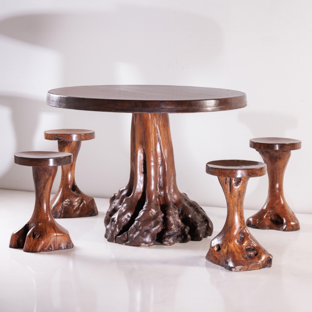 A round olive wood table with a natural tree root pedestal base surrounded by four matching root wood stools. View VI