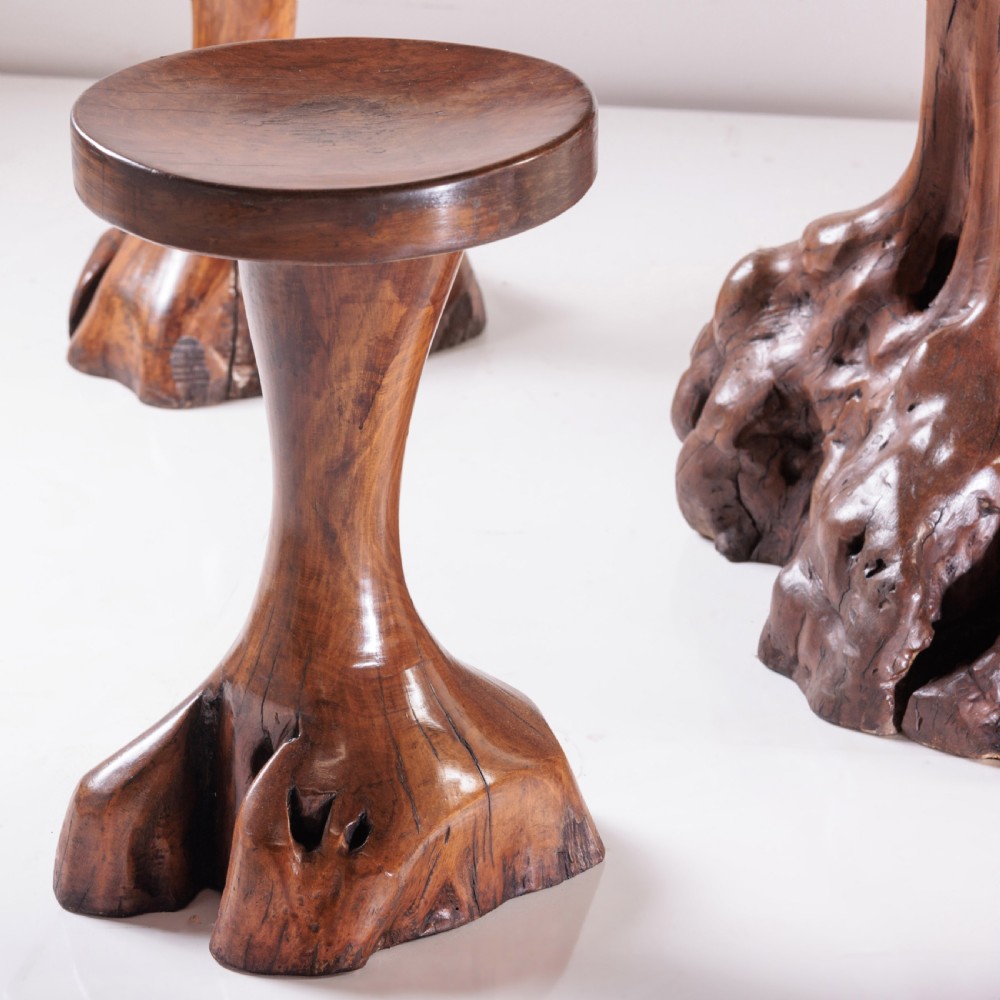 A round olive wood table with a natural tree root pedestal base surrounded by four matching root wood stools. View VII