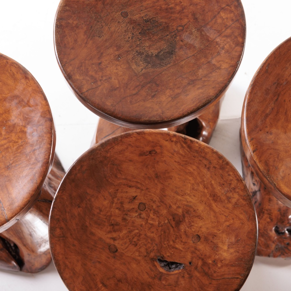 A round olive wood table with a natural tree root pedestal base surrounded by four matching root wood stools. View X