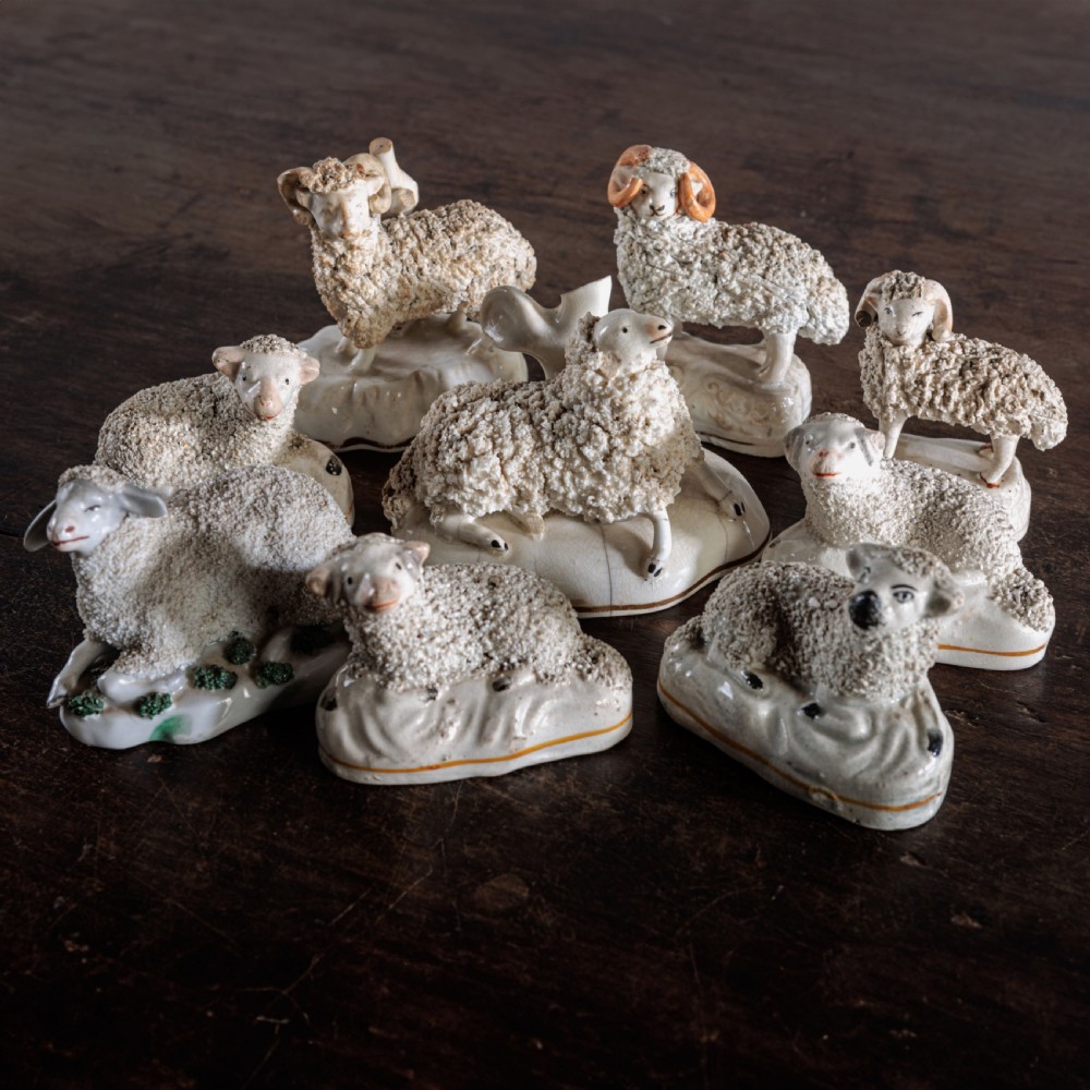 A collection of eight antique 19th-century cream and white ceramic Staffordshire sheep and lamb figurines with textured shredded-clay fleece.