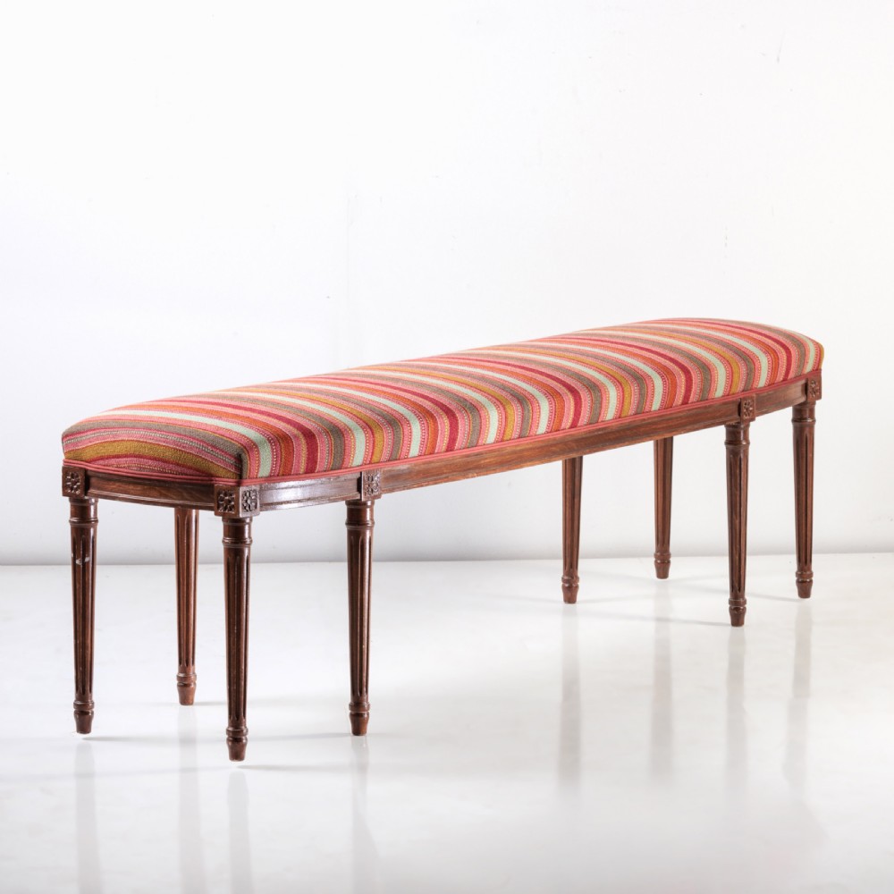 A long nineteenth-century French bench featuring a multi-coloured striped upholstered seat supported by eight fluted dark wood legs with carved rosettes.