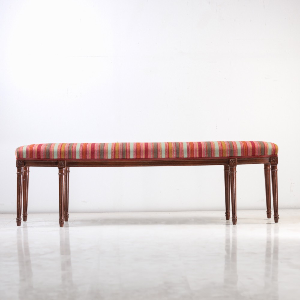 A long nineteenth-century French bench featuring a multi-coloured striped upholstered seat supported by eight fluted dark wood legs with carved rosettes. View II