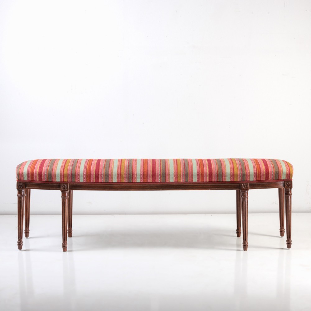 A long nineteenth-century French bench featuring a multi-coloured striped upholstered seat supported by eight fluted dark wood legs with carved rosettes. View III