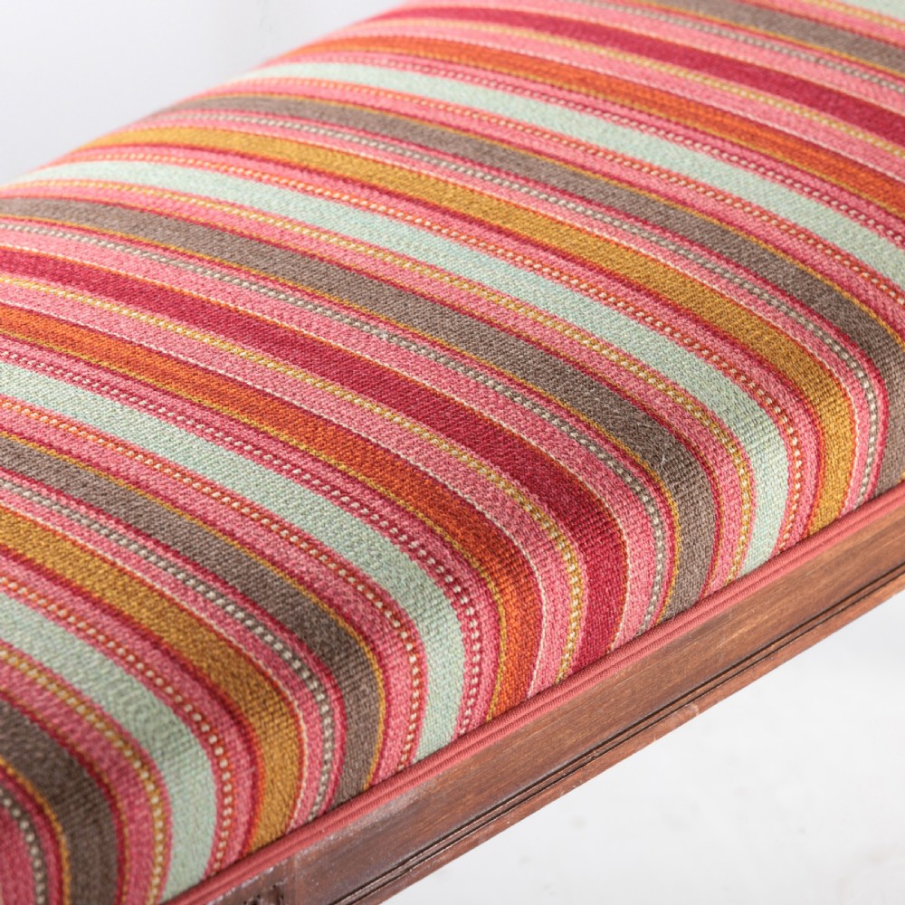 A long nineteenth-century French bench featuring a multi-coloured striped upholstered seat supported by eight fluted dark wood legs with carved rosettes. View V