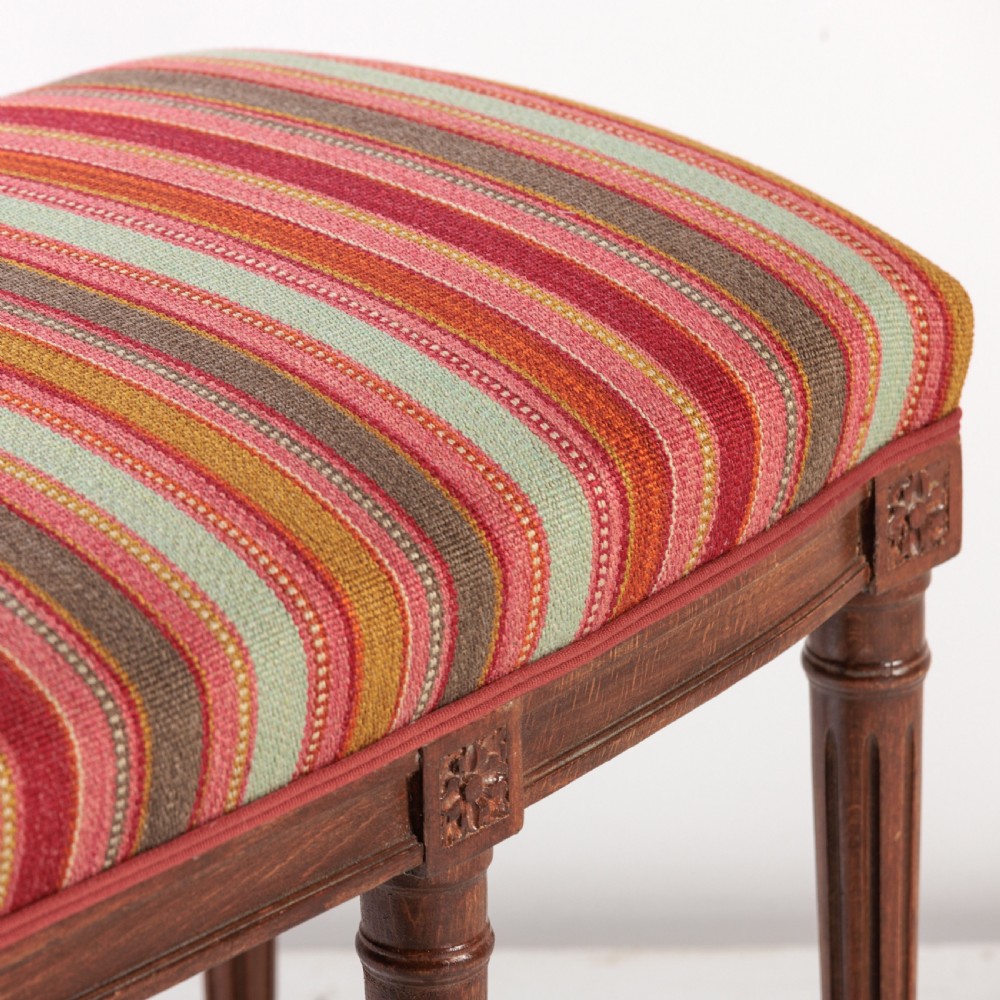 A long nineteenth-century French bench featuring a multi-coloured striped upholstered seat supported by eight fluted dark wood legs with carved rosettes. View VI