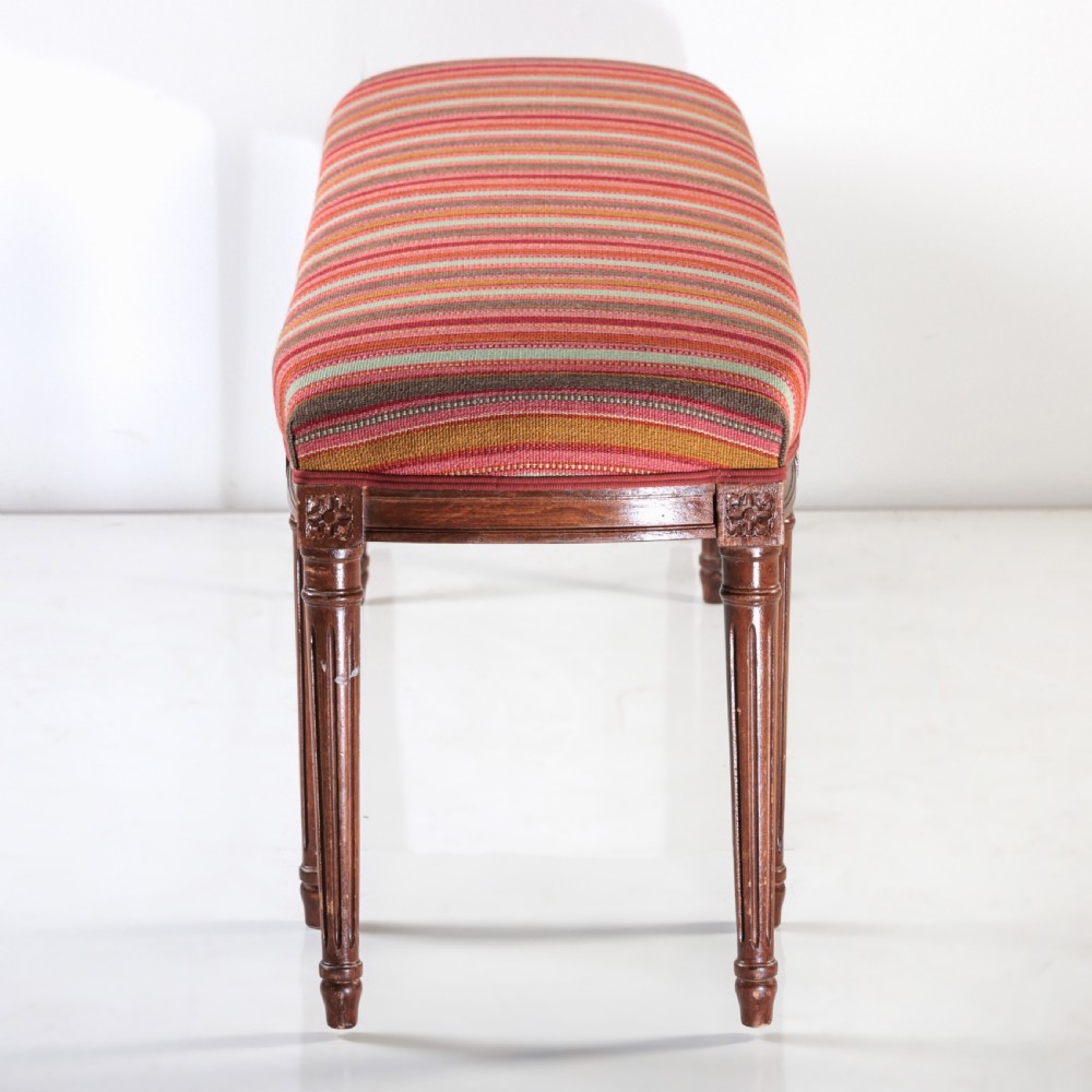 A long nineteenth-century French bench featuring a multi-coloured striped upholstered seat supported by eight fluted dark wood legs with carved rosettes. View VII
