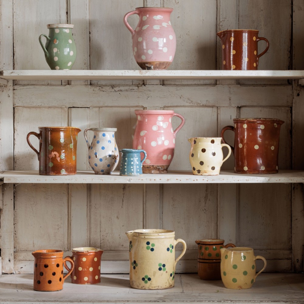 A collection of twelve 19th-century earthenware jugs in varying sizes and colours, each decorated with hand-painted spot and polka dot motifs.
