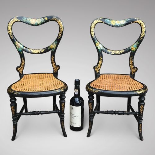 fig 1. A pair of small Victorian black lacquered papier-mache chairs featuring heart-shaped backrests with floral paintwork, gilt foliage detailing, and woven cane seats.