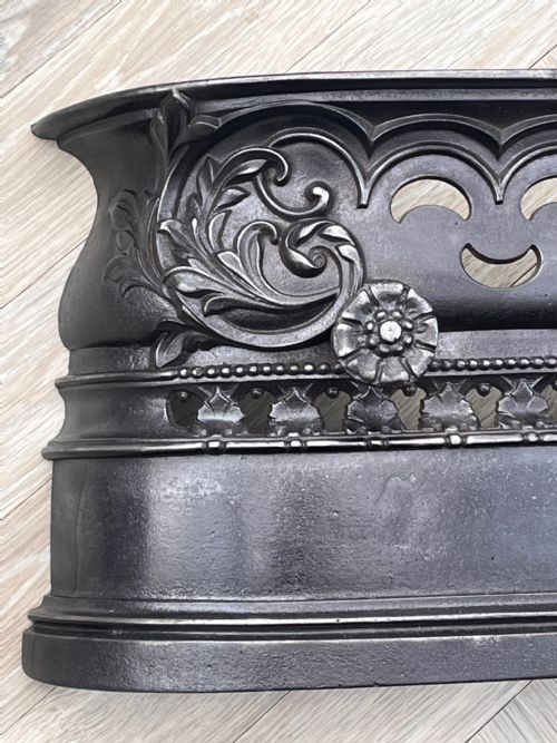 fig 1. A Victorian cast iron fireplace fender featuring openwork scroll detailing, floral rosette accents, and a curved top rim.