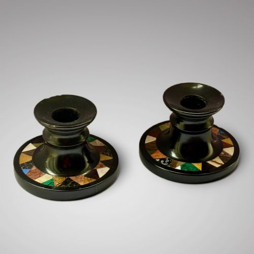 fig 1. A pair of turned Ashford black marble candlesticks featuring geometric specimen stone inlays around circular bases, fitted with cream taper candles.