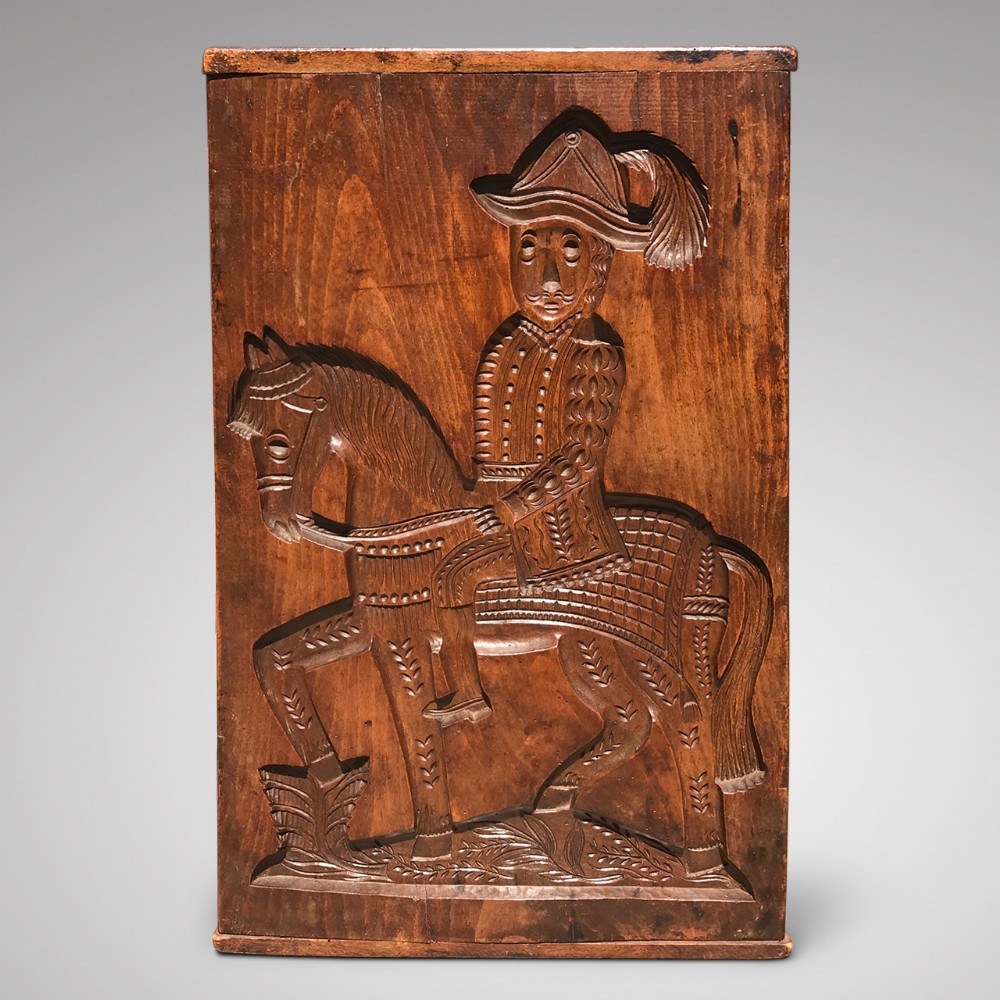 A rectangular hand-carved timber board depicting a high-relief figure of a man in a feathered hat riding a saddled horse.