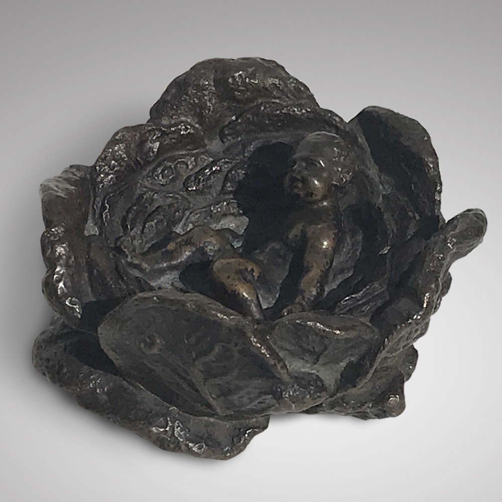 A 19th-century dark bronze desk weight sculpted in the form of an infant resting inside an open cabbage head.