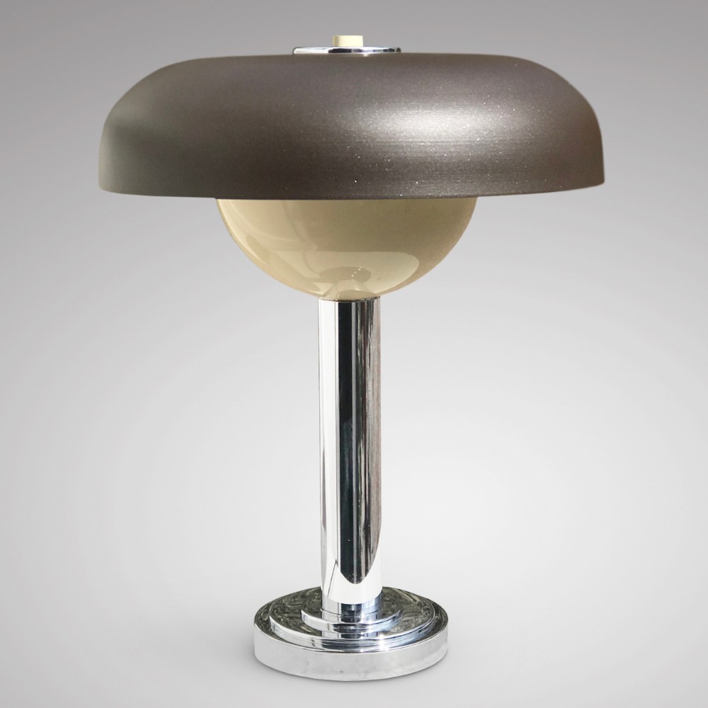 An Art Deco style table lamp featuring a chrome cylindrical stem on a stepped circular base, topped with a cream bowl accent and a broad dark brown metal dome shade.