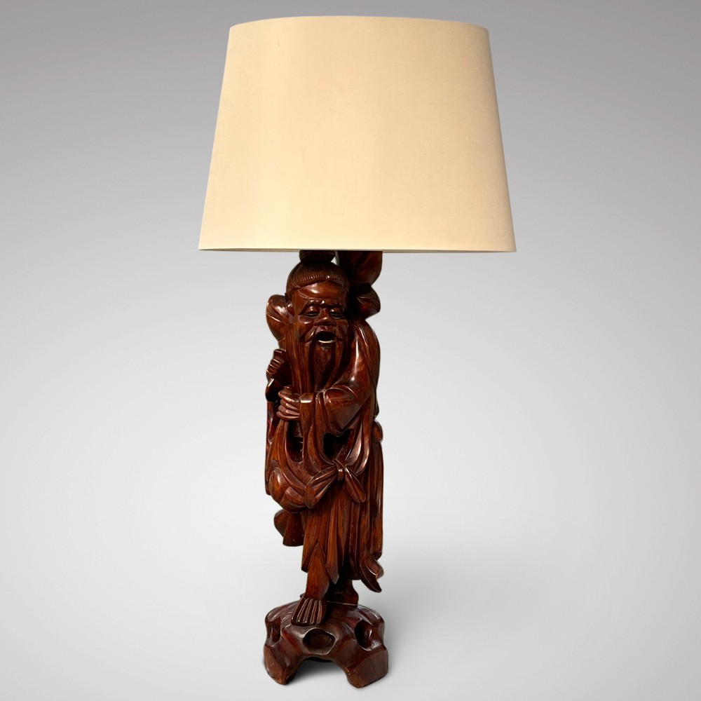 A 19th-century Japanese table lamp featuring a dark brown hand-carved root wood figure of a bearded sage, paired with a cream fabric lampshade.