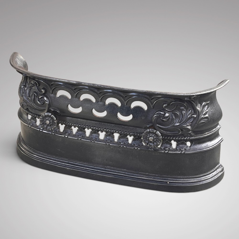 A Victorian cast iron fireplace fender featuring openwork scroll detailing, floral rosette accents, and a curved top rim.