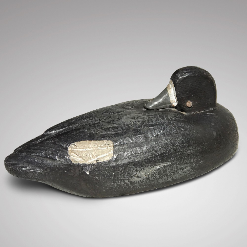 An early 20th century carved wooden decoy duck with a painted black finish and a pale distressed patch on its side.