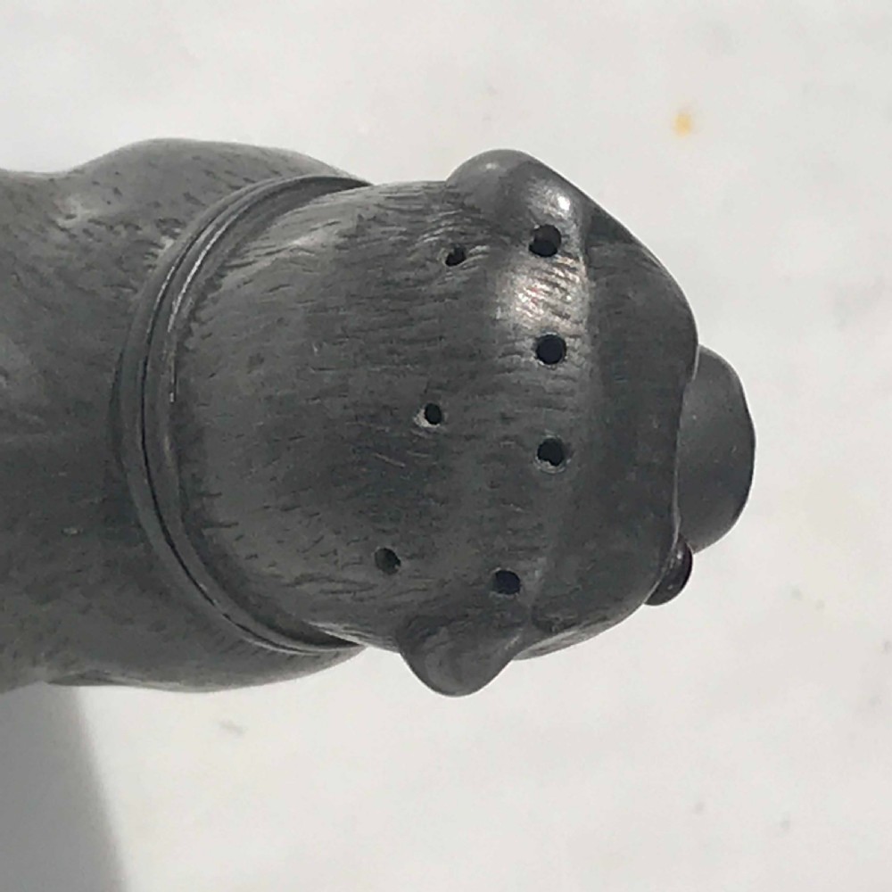 A 19th-century cast pewter pepperette shaped as a seated dog with red glass eyes and pierced holes at the snout. View VI