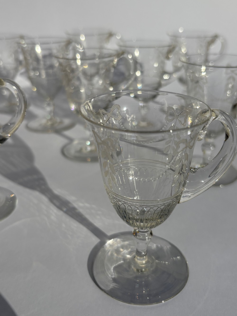 A set of clear Victorian stemmed glass custard cups featuring etched bow motifs and curved side handles.