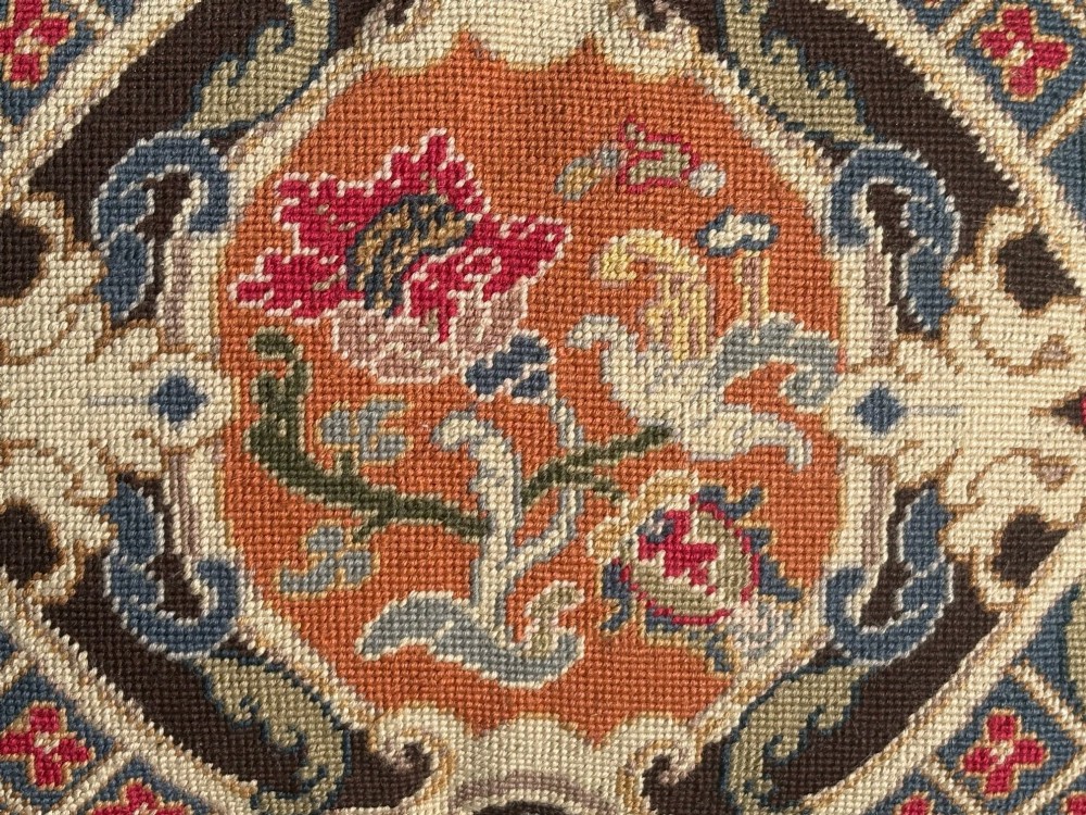 A rectangular wool needlepoint cushion featuring a central floral medallion in terracotta and cream surrounded by scrollwork and finished with a fringed border. View II