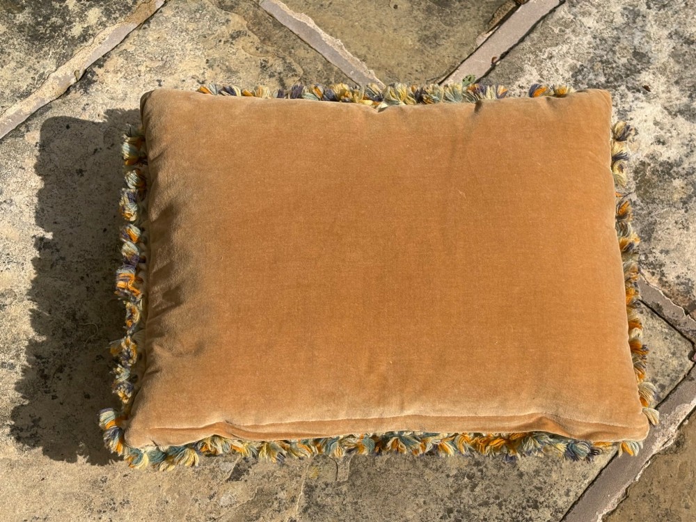 A rectangular wool needlepoint cushion featuring a central floral medallion in terracotta and cream surrounded by scrollwork and finished with a fringed border. View III