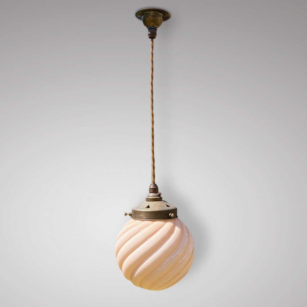 An Art Deco pendant light featuring a pale pink swirl-patterned opaline glass globe shade with an aged brass gallery and suspended flex.