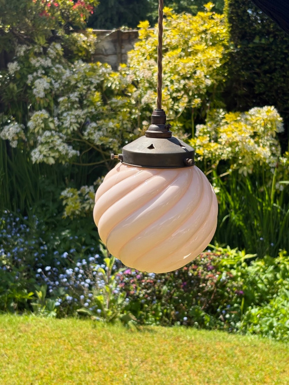An Art Deco pendant light featuring a pale pink swirl-patterned opaline glass globe shade with an aged brass gallery and suspended flex. View II