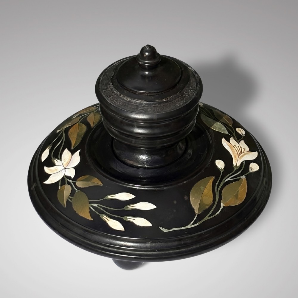 A circular black marble inkwell stand featuring detailed floral hardstone inlays and a central covered ink pot.