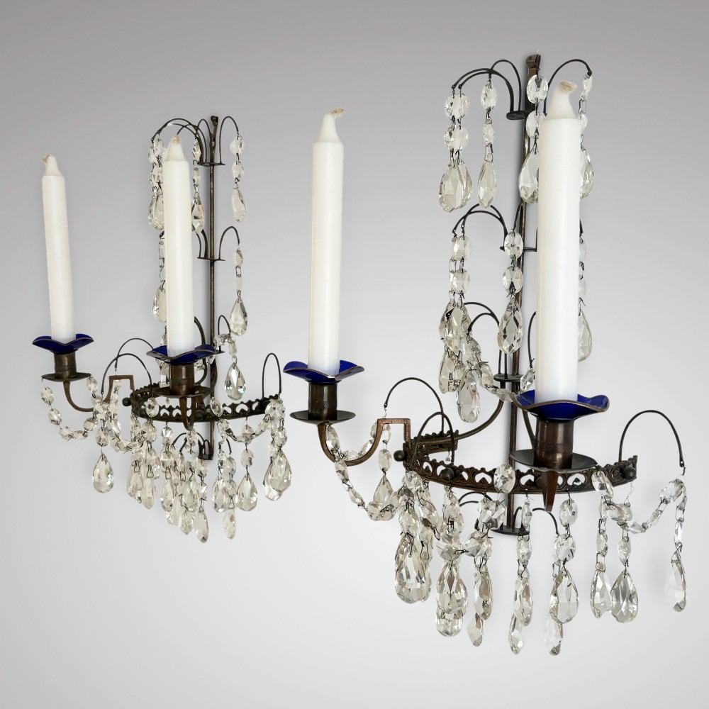 A pair of Swedish antique wall sconces featuring dark brass frames, cascading cut crystal drops, and blue glass drip pans holding white candles. View II
