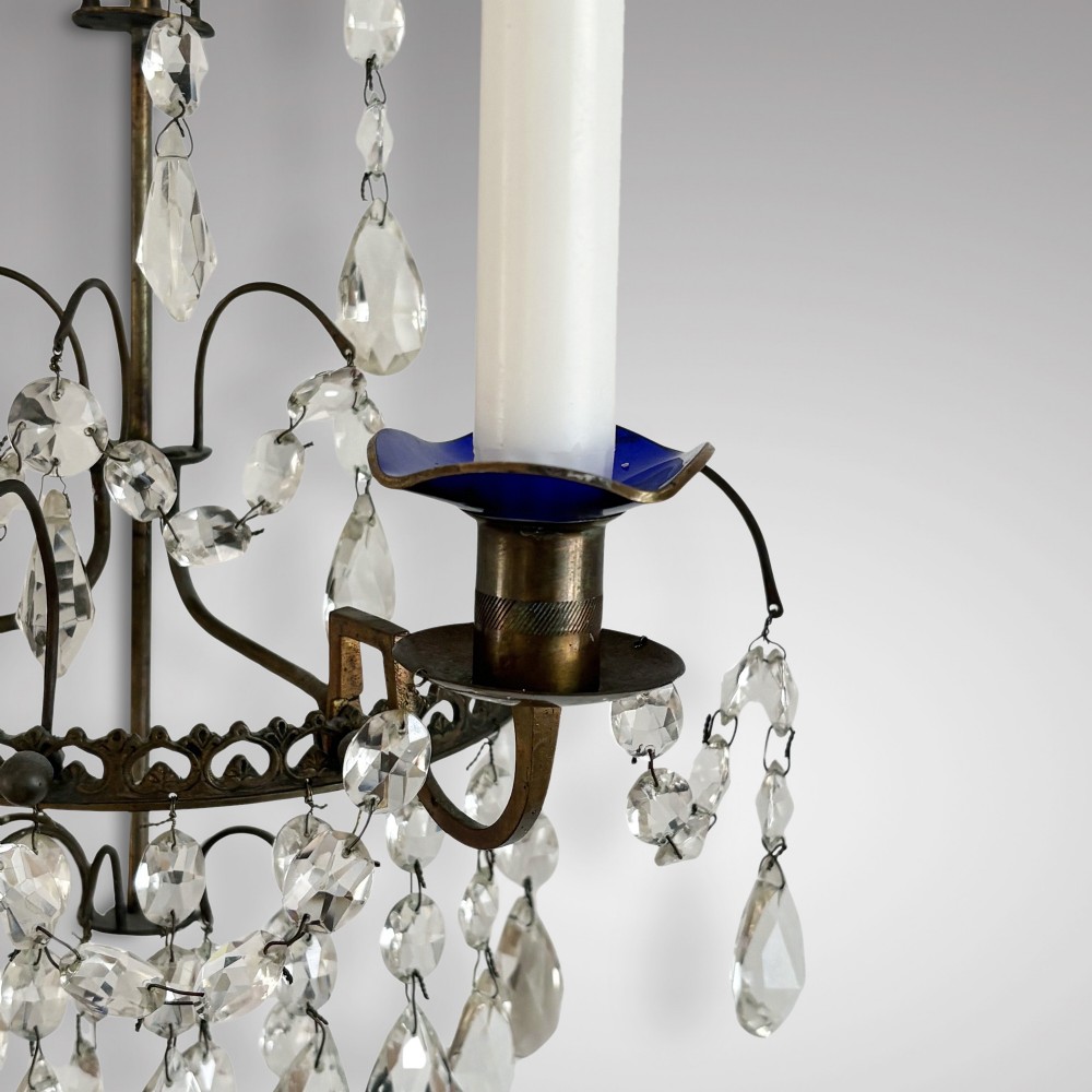 A pair of Swedish antique wall sconces featuring dark brass frames, cascading cut crystal drops, and blue glass drip pans holding white candles. View III