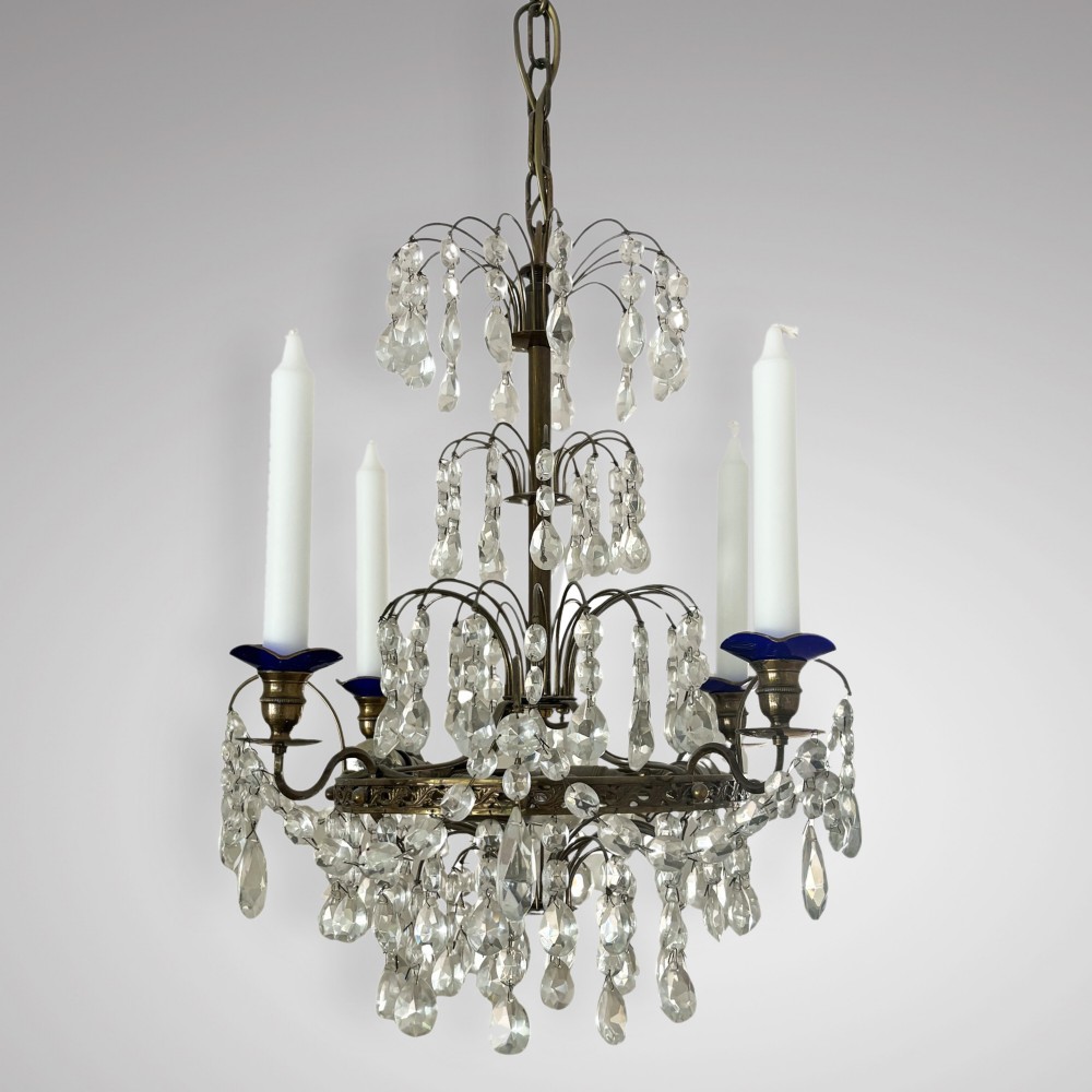 An antique Swedish crystal chandelier featuring tiered wire rings with cascading glass drops, brass candle sconces with blue glass accents, and white taper candles.
