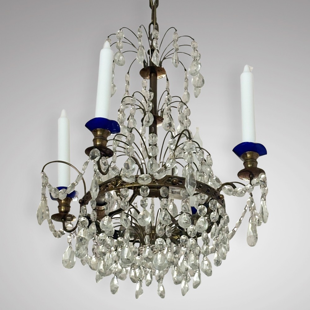 An antique Swedish crystal chandelier featuring tiered wire rings with cascading glass drops, brass candle sconces with blue glass accents, and white taper candles. View II