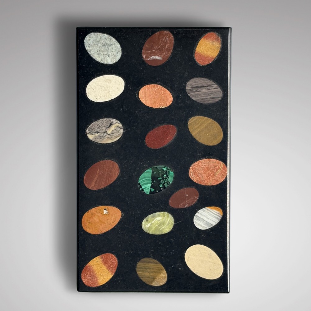 A rectangular black marble paperweight inlaid with twenty oval polished stone specimens of various colours arranged in a grid pattern. View II