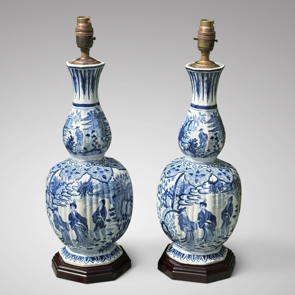 A pair of 19th-century blue and white Delftware ceramic table lamps with hand-painted figurative scenes, mounted on dark timber bases with cream scalloped shades. View II