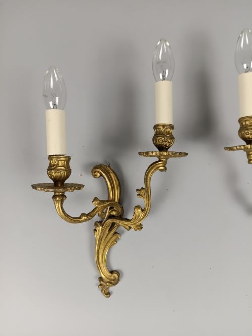 fig 1. A pair of French gilt brass two-arm wall sconces featuring ornate acanthus leaf scrollwork and faux candle sleeve fittings.