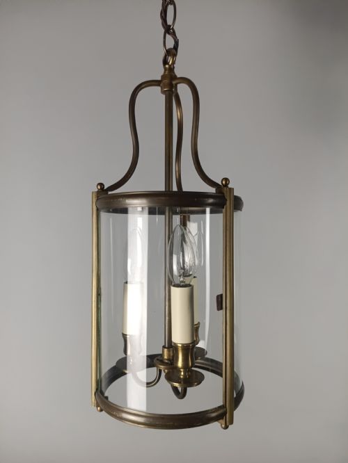 fig 2. A cylindrical gilded brass hall lantern featuring curved clear glass panels and an internal three-light candle cluster.