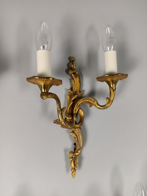 fig 2. Four French Rococo style gilded bronze twin-arm wall lights with foliate scrollwork and white candle sleeves.
