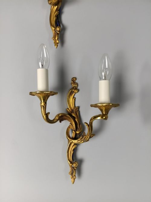 fig 3. Four French Rococo style gilded bronze twin-arm wall lights with foliate scrollwork and white candle sleeves.