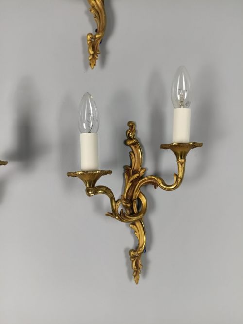 fig 4. Four French Rococo style gilded bronze twin-arm wall lights with foliate scrollwork and white candle sleeves.