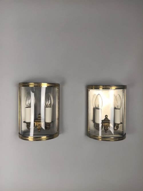 fig 1. A pair of French gilt brass half-lantern wall lights featuring curved clear glass panels and twin candle-style sockets.